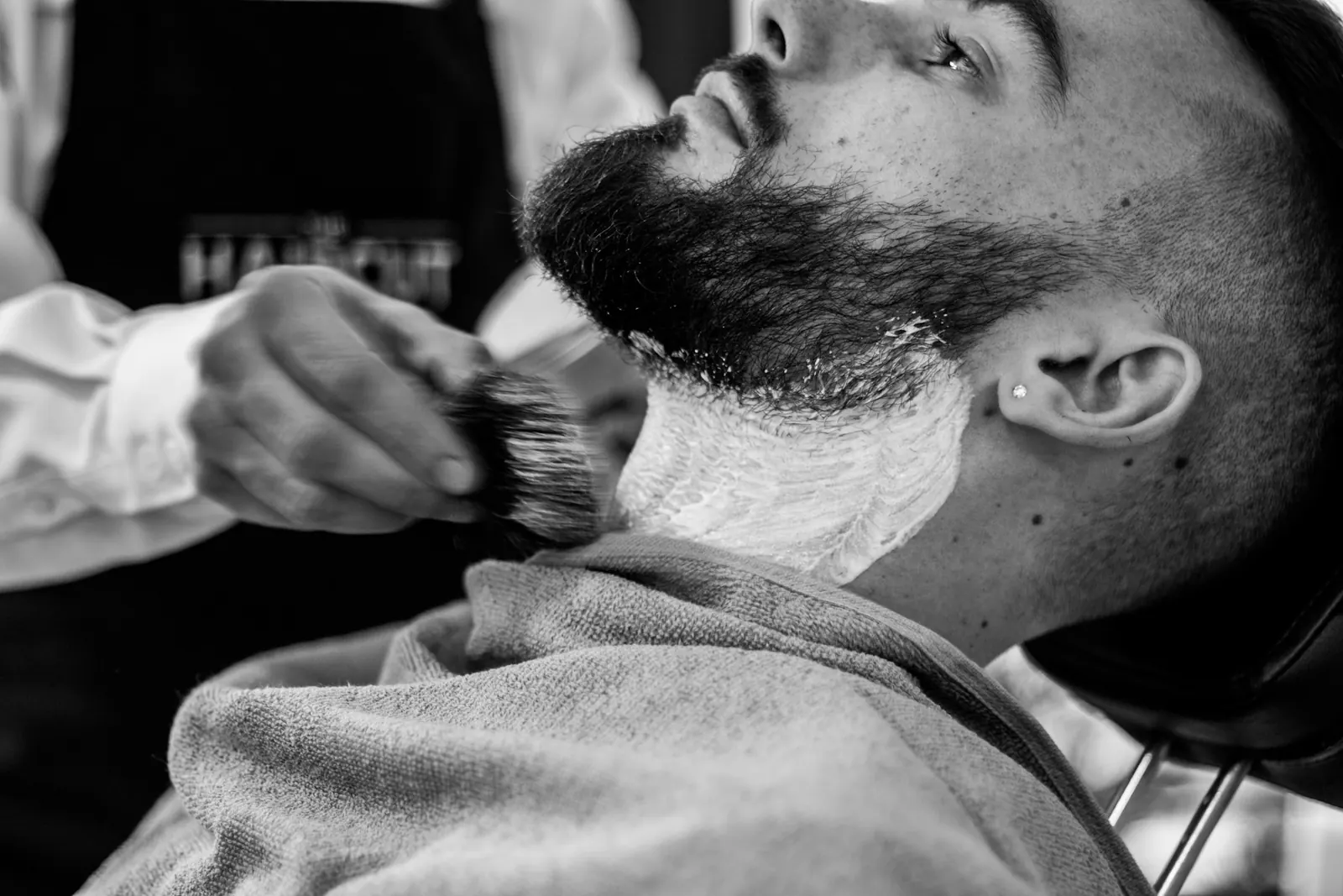 Il barbiere stende la schiuma sulla barba di un cliente, in bianco e nero